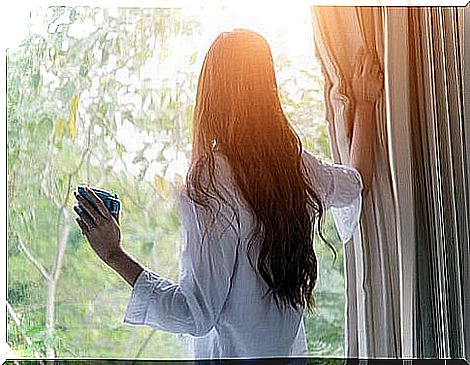 Woman looking out the window with coffee in hand.